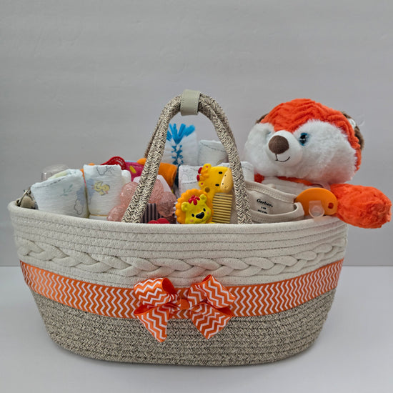 Little Fox diaper caddy gift basket, a woven rope caddy with orange chevron ribbon and bow, a plush fox, diapers and baby essentials