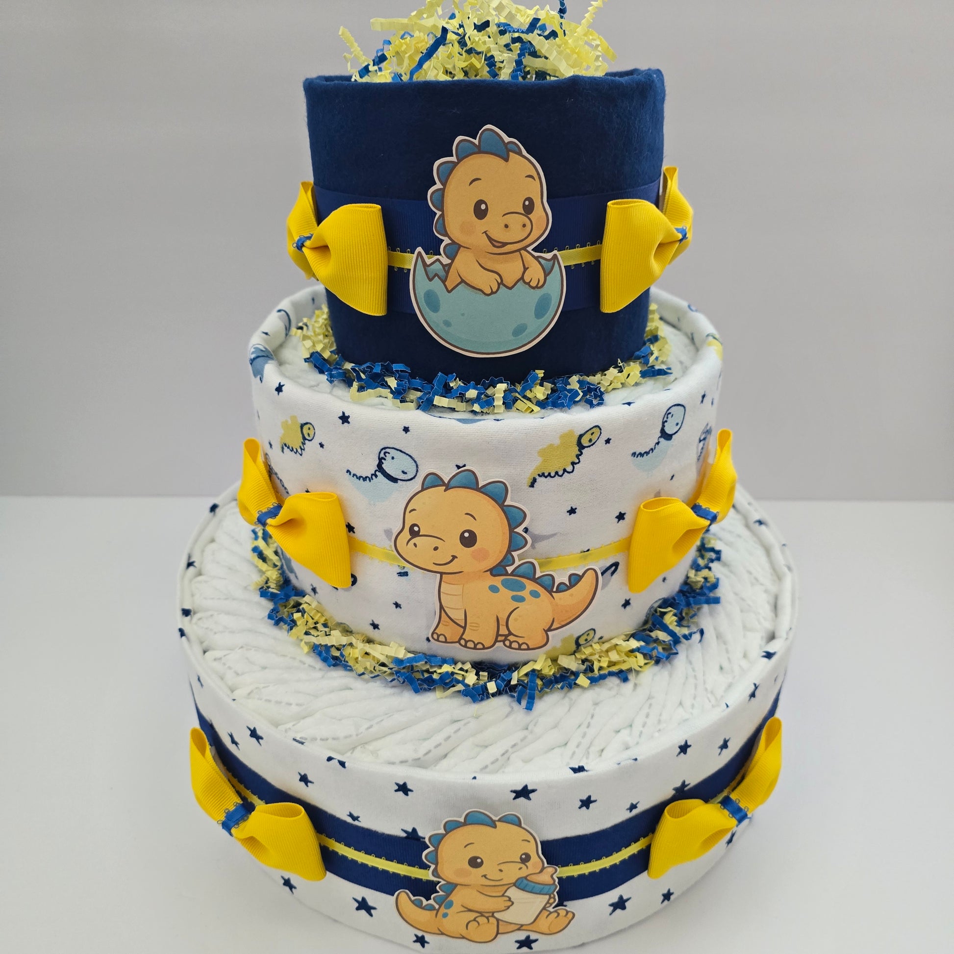 "Handmade baby dinosaur diaper cake with plush dino toy, green ribbon, and diapers, perfect baby shower centerpiece or gift"