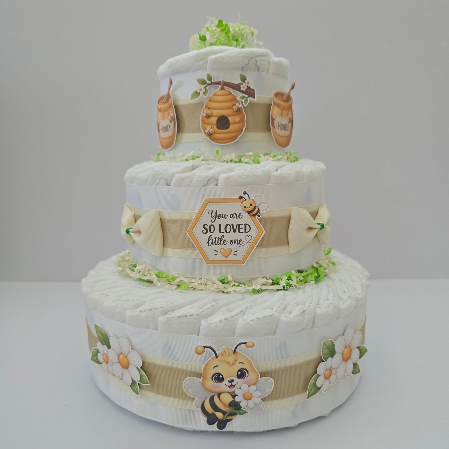 Sweet as Can Bee three-tier diaper cake made with premium Size 1 diapers, soft neutral ribbons, adorable bee, honey and floral decorations, displayed at a beautiful bee-themed baby shower