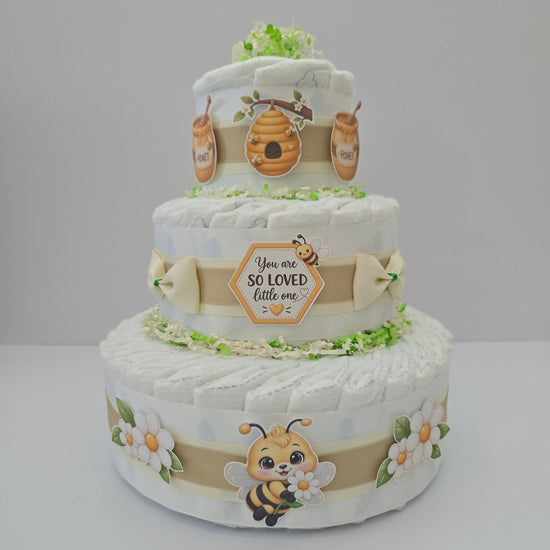 Sweet As Can Bee diaper cake with three tiers, soft neutral ribbons, a bumblebee, beehive and honey accents, white flowers and greenery
