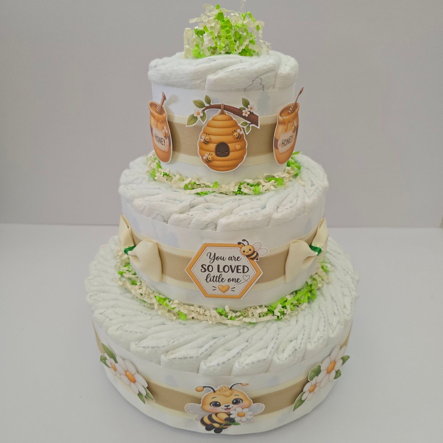 Sweet as Can Bee three-tier diaper cake made with premium Size 1 diapers, soft neutral ribbons, adorable bee, honey and floral decorations, displayed at a beautiful bee-themed baby shower