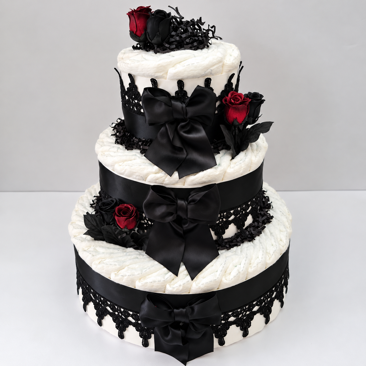 3-tier Gothic baby shower diaper cake with 50 premium diapers, black satin bows, lace trim, and burgundy and black roses by Fine Diaper Cakes.